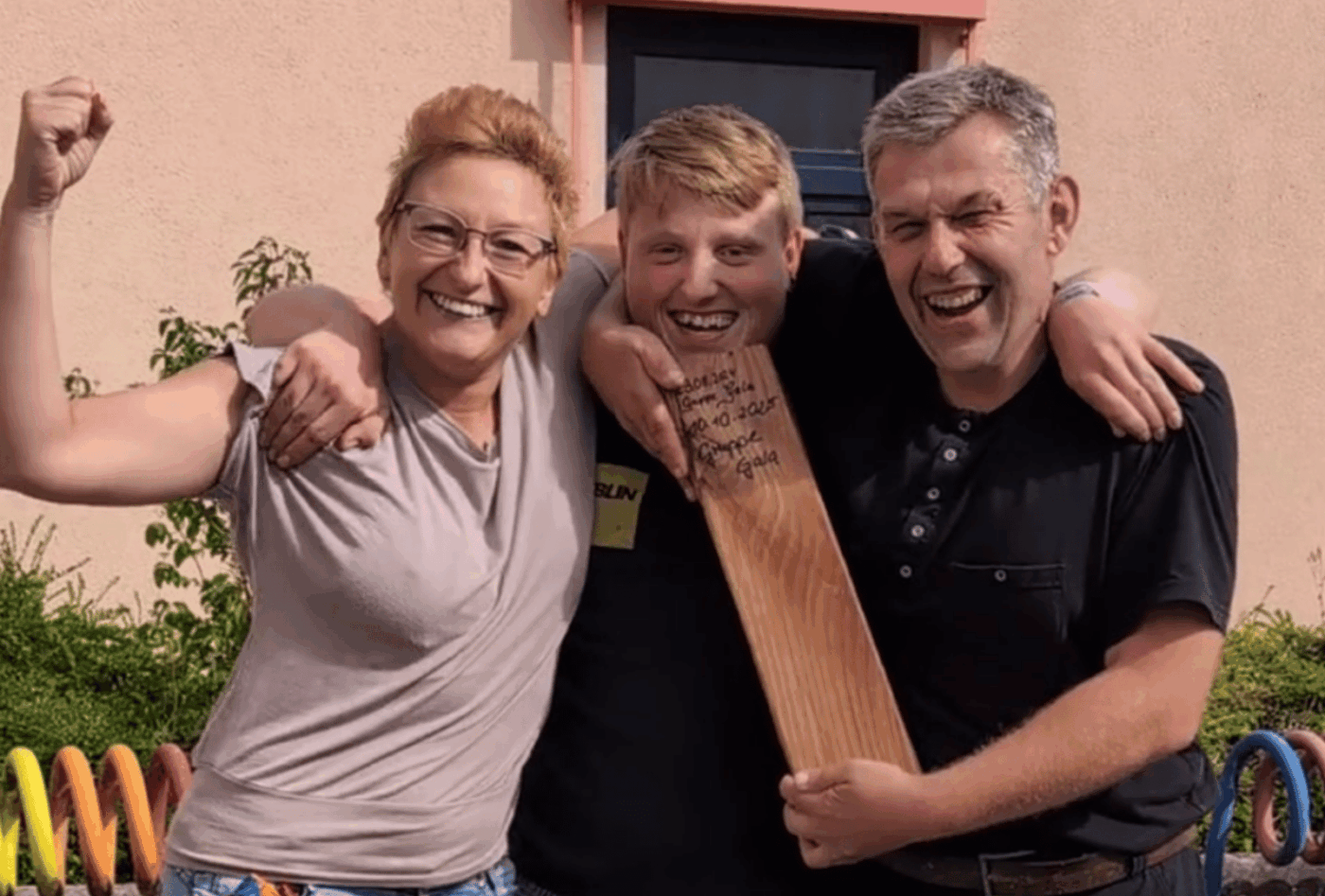 Drei Menschen feiern gemeinsam den Sieg der Gruppe GALA beim Wikingerschach. Der Mann in der Mitte hält den Holzpreis.