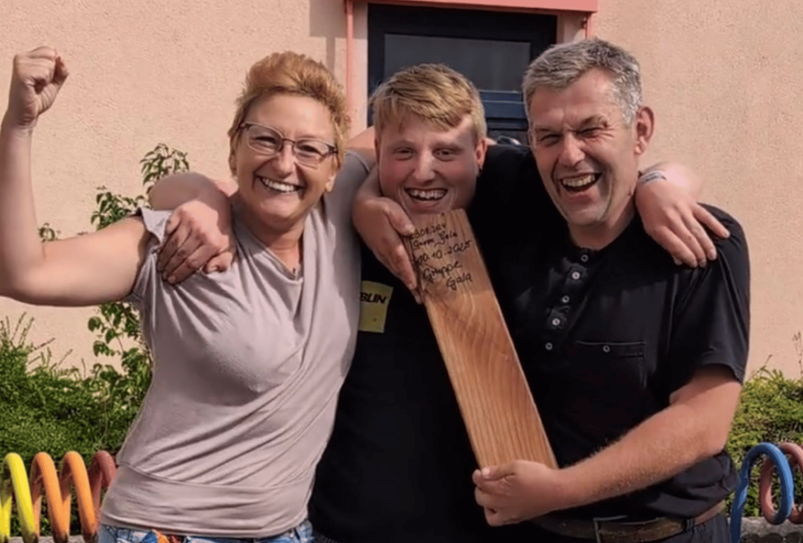 Drei Menschen feiern gemeinsam den Sieg der Gruppe GALA beim Wikingerschach. Der Mann in der Mitte hält den Holzpreis.