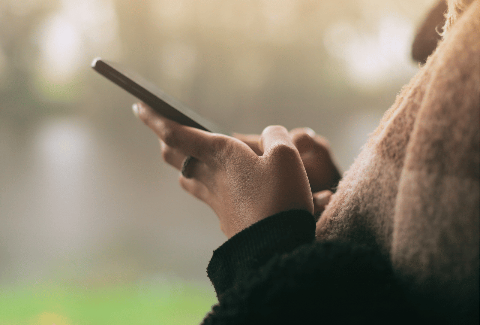 Nahaufnahme einer Person, die im Freien ein Smartphone bedient. Der Hintergrund ist weich verschwommen.